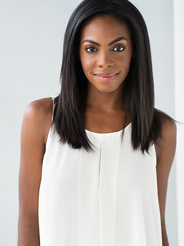 A woman with long black hair is smiling and wearing a sleeveless white top. She is standing against a light background.